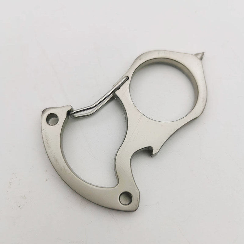 Bare steel version of the carabiner keychain tool on a white surface, showing the spring gate, round finger hole, bottle opener notch, countersunk handle holes and pointed tip