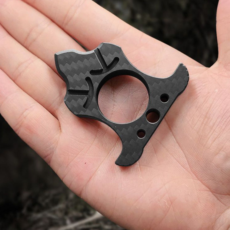 Triangular carbon fiber knuckle with a central finger hole, claw prongs and a bottle-opener hook at the base, resting in an open palm.