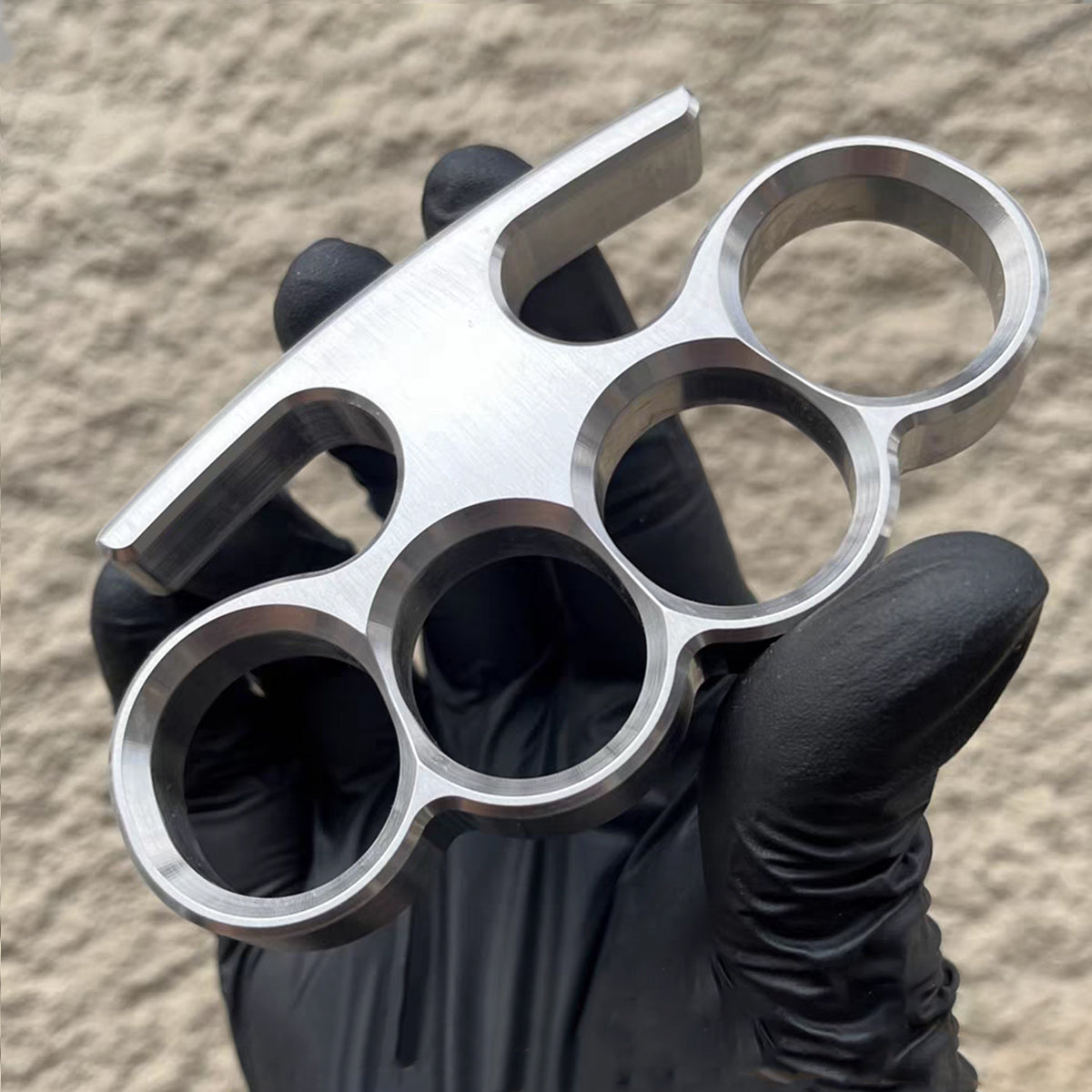 Black-gloved hand holding the 304 stainless steel classic knuckle duster at rest.