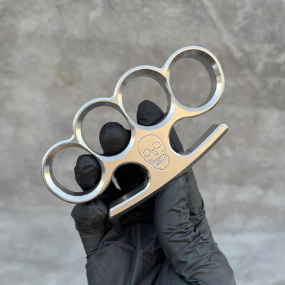 The 304 stainless steel classic knuckle duster stands upright between a black-gloved thumb and fingers.