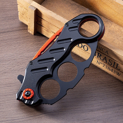 Closed black folding knuckle knife leaning against wooden box, alternate view