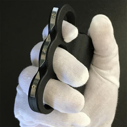 Close-up of a white-gloved hand gripping the black three-hole stun device, three steel prong plates with pointed tips and mounting screws along the front edge
