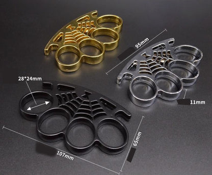 Three cobweb knuckle dusters in gold, black and silver shown with yellow dimension markings - 107 mm wide, 65 mm tall, 11 mm thick and a 28 x 24 mm finger hole - on a dark gray surface.