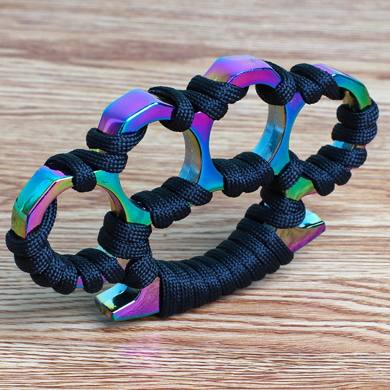 Colorful rainbow-finish woven knuckle duster on a wooden table with black umbrella rope around the openings and palm base