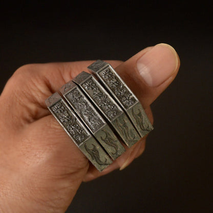 Dark silver stacked hexagon rings with green patina worn on a finger, engraved characters and flame motifs visible