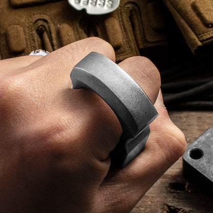 Dark single-hole knuckle weight worn on one finger, showing the flat body seated against the hand