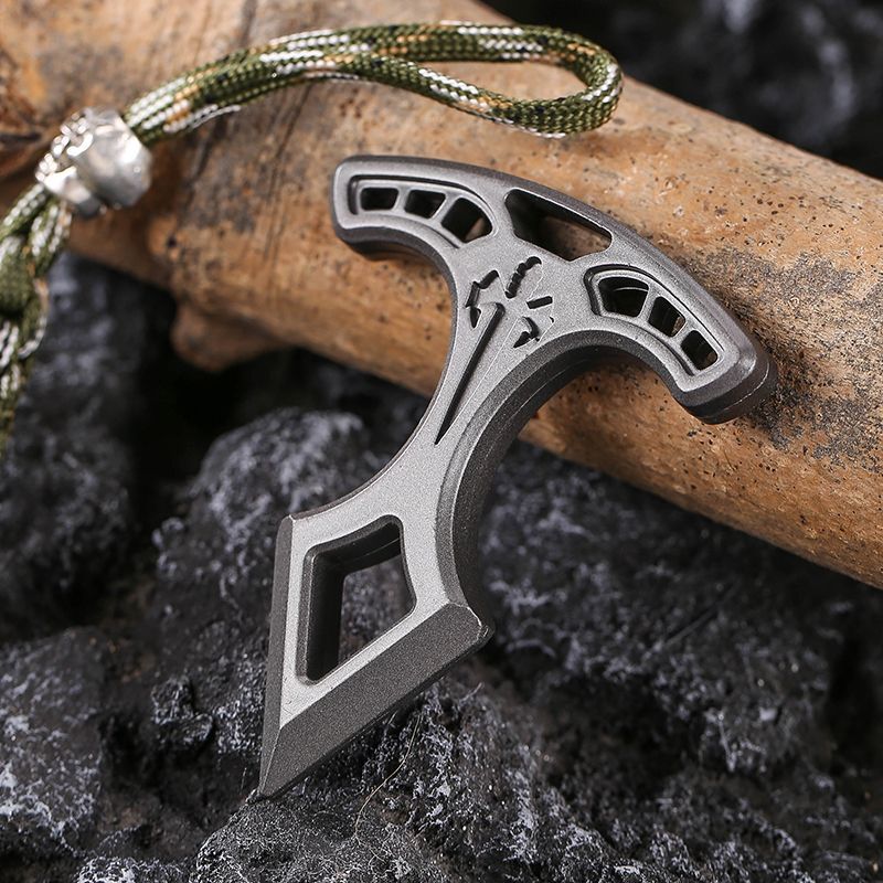 Metal pendant resting on dark rocks with its camo paracord lanyard stretching away at the top.