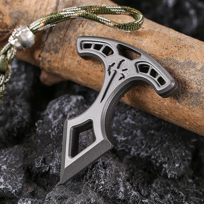 Metal pendant resting on dark rocks with its camo paracord lanyard stretching away at the top.