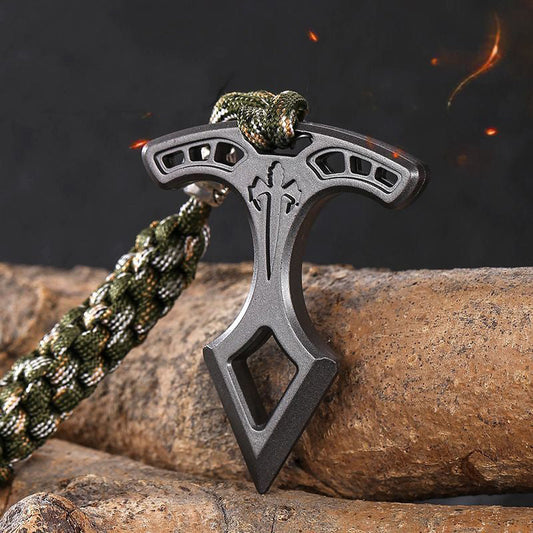 Spear head EDC pendant standing upright on a log with embers in the background, showing the slotted bar and pointed tip.