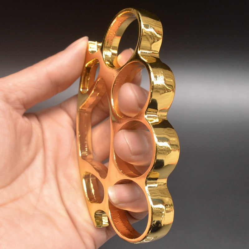 Gold knuckle duster with window breaker held in hand showing side profile