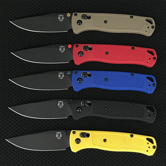 Five folding knives with black-coated drop-point blades and textured handles in tan, red, blue, black and yellow arranged on a dark mat