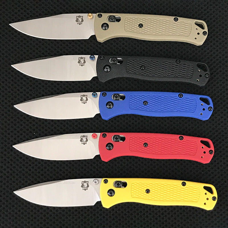 Five folding knives with satin silver drop-point blades and textured handles in tan, black, blue, red and yellow lined up in rows