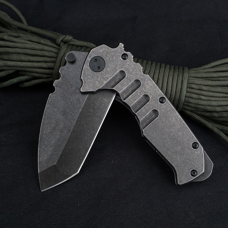 A partially open folding knife resting on olive paracord, showing the stonewashed blade at an angle to its grooved steel handle, with a dark pivot where the blade meets the handle.