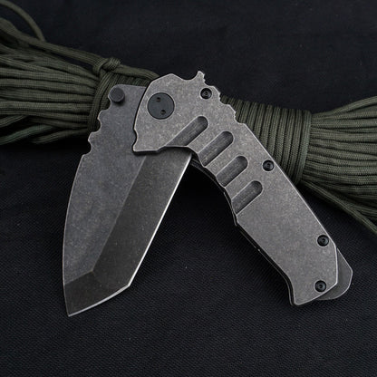 A partially open folding knife resting on olive paracord, showing the stonewashed blade at an angle to its grooved steel handle, with a dark pivot where the blade meets the handle.