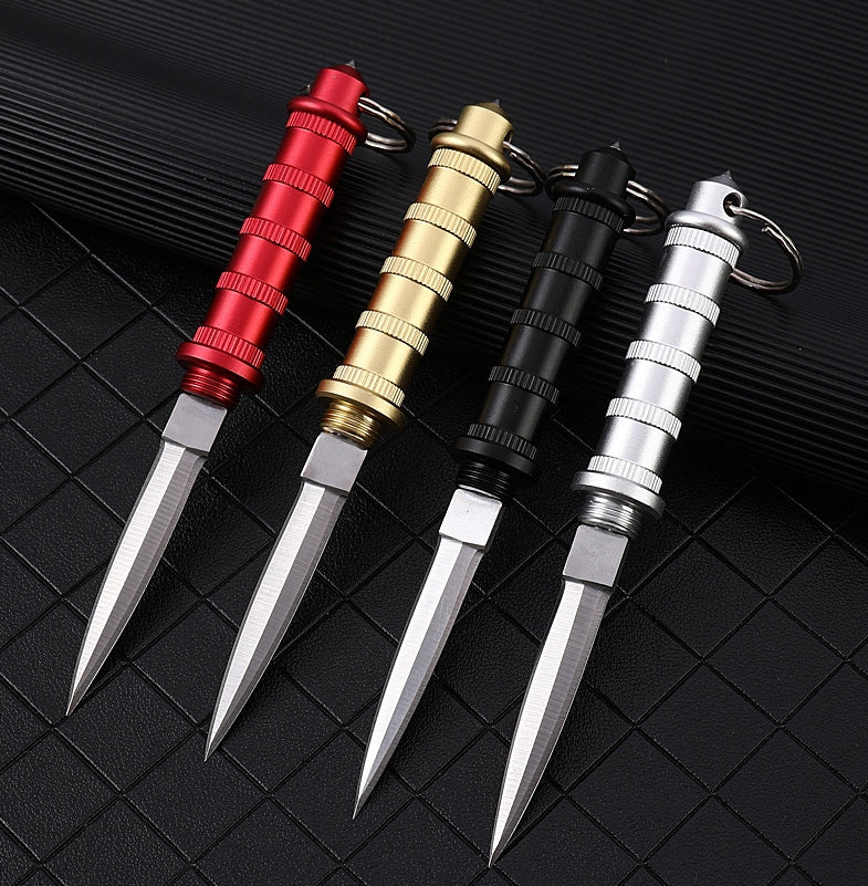 Four keychain daggers in Red, Gold, Black and Silver seen from above, blades exposed with chisel grinds, ribbed handles and keyrings.