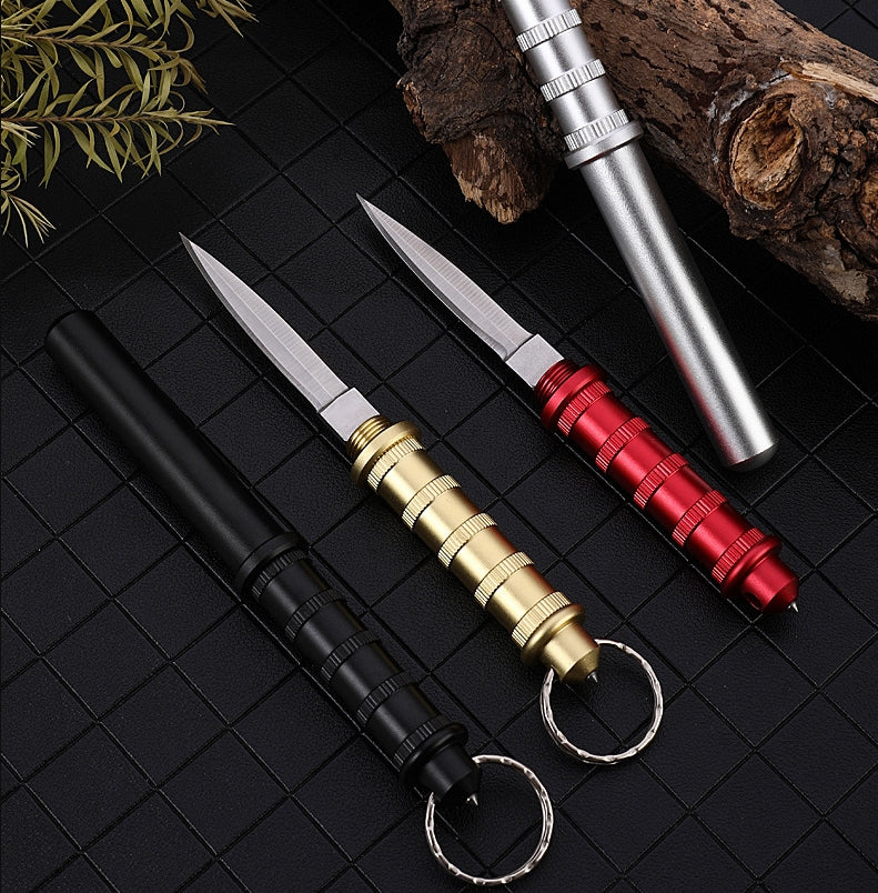 Four keychain daggers on a black grid — Gold and Red open with blades out, Black and Silver closed with blades hidden, ribbed handles and keyrings.