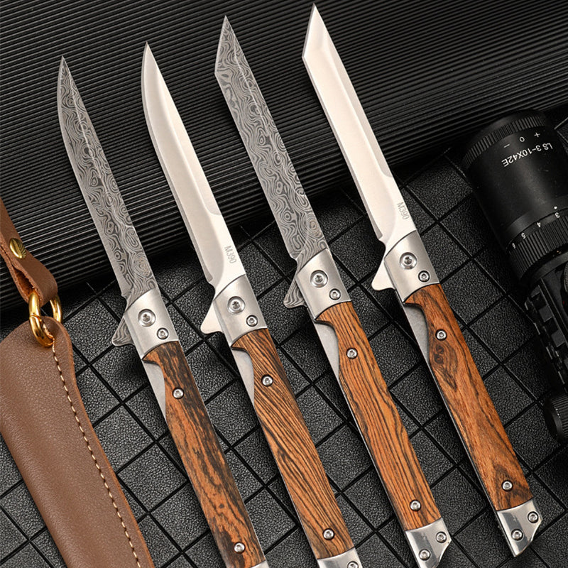 Four open folding knives fanned in a row with striped wood handles, showing Damascus-pattern and plain stainless blades including one angular-tip blade, a leather sheath at the left edge and a black flashlight at the right