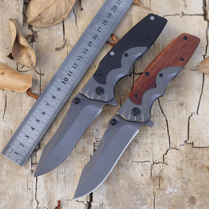 G10-handle and wood-handle folding knives open side by side beside a metal ruler