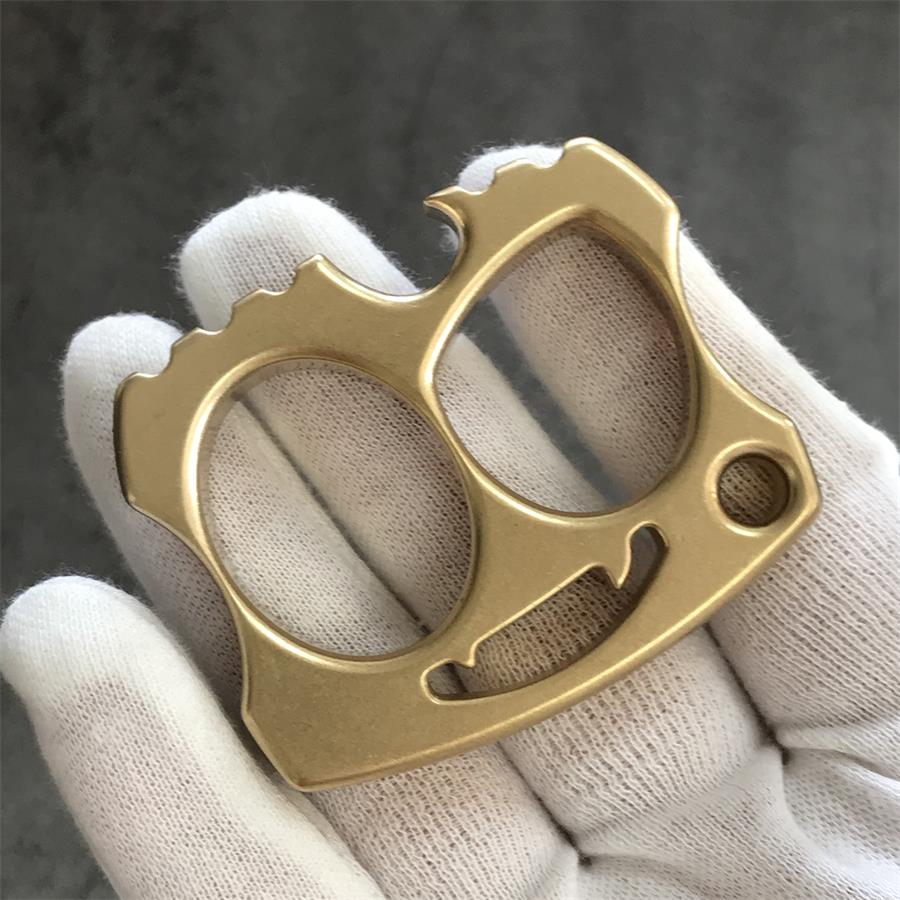 Gloved hand holding brass two-hole knuckle angled to show smile cutout
