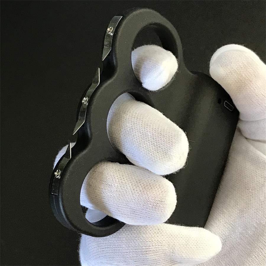 White-gloved hand holding the black three-hole stun device showing three serrated steel prong plates fixed with screws along the front edge