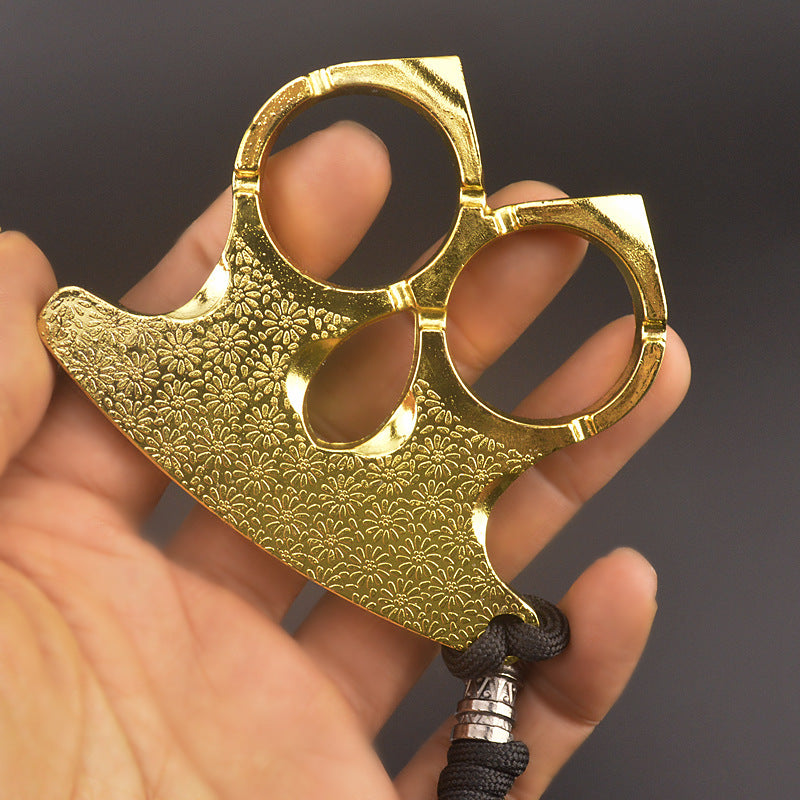Polished gold two-finger knuckle held in an open hand, engraved flowers and cord bead in view