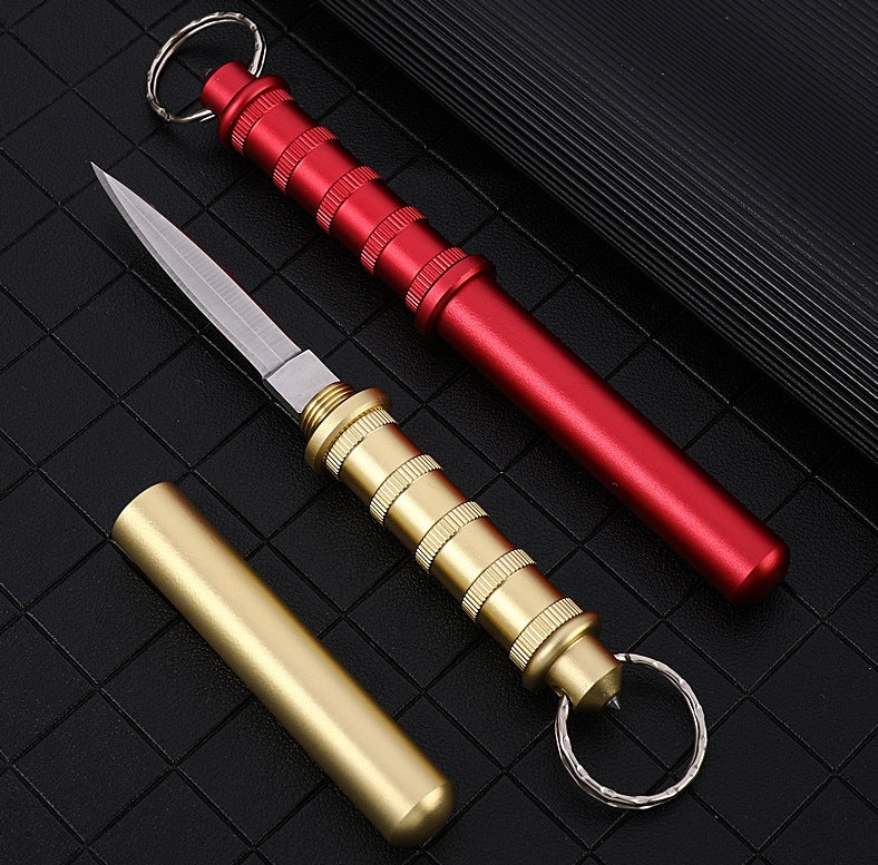 Gold and Red keychain daggers on a black grid — Gold shown with the blade out beside its cap, Red closed with the blade tucked into the handle.
