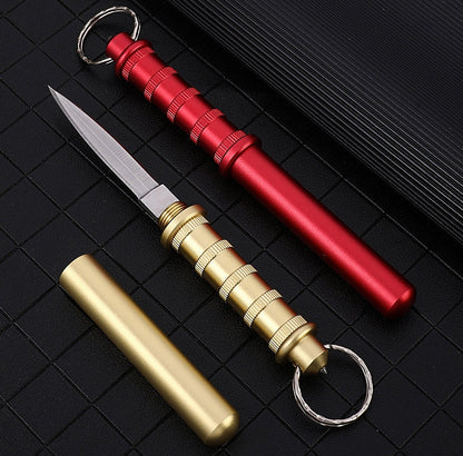 Gold and Red keychain daggers on a black grid — Gold shown with the blade out beside its cap, Red closed with the blade tucked into the handle.