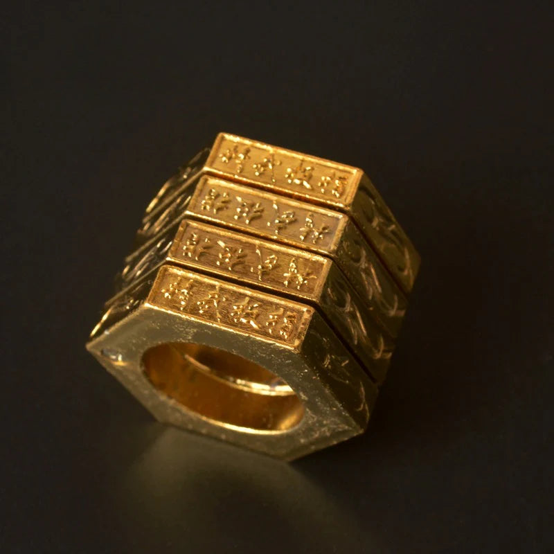 Gold stacked hexagon ring standing upright on a dark background with engraved characters on every band