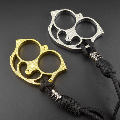 Golden and silver two-finger sloth knuckle pieces side by side, each threaded with a black paracord lanyard and engraved metal bead on a dark grey background