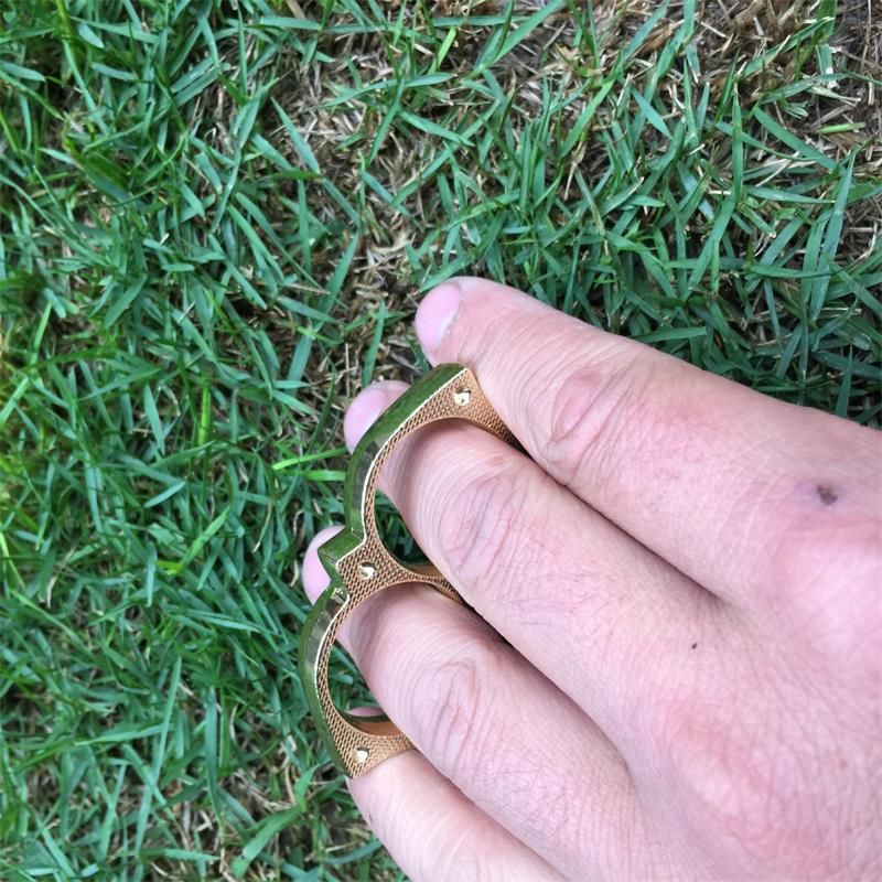 Golden sloth finger clasp worn on two fingers over grass showing the finger holes and outdoor carry