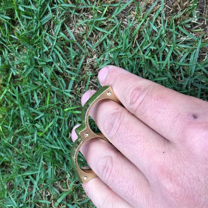 Golden sloth finger clasp worn on two fingers over grass showing the finger holes and outdoor carry