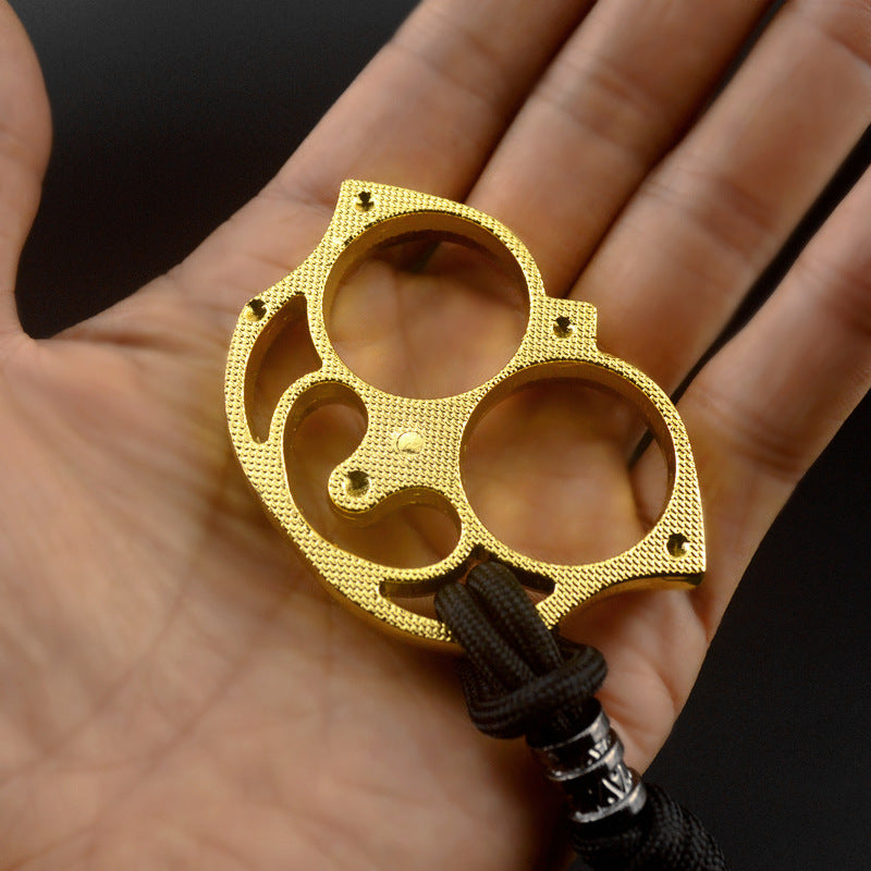 Golden two-finger sloth piece lying in an open palm showing the full sloth face outline, two finger holes and black paracord lanyard