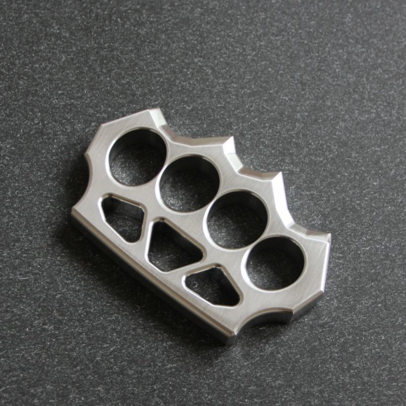 304 stainless steel grass shaped knuckle duster with four finger holes and decorative cutouts on a dark surface.