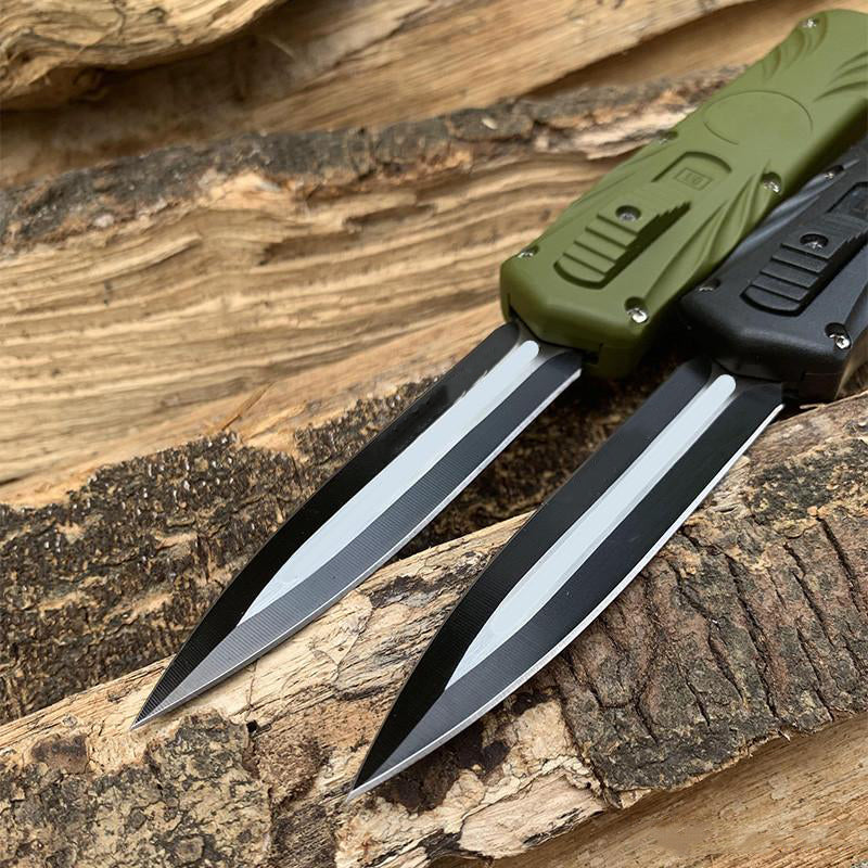 Green and black automatic OTF pocket knives crossed on rough tree bark
