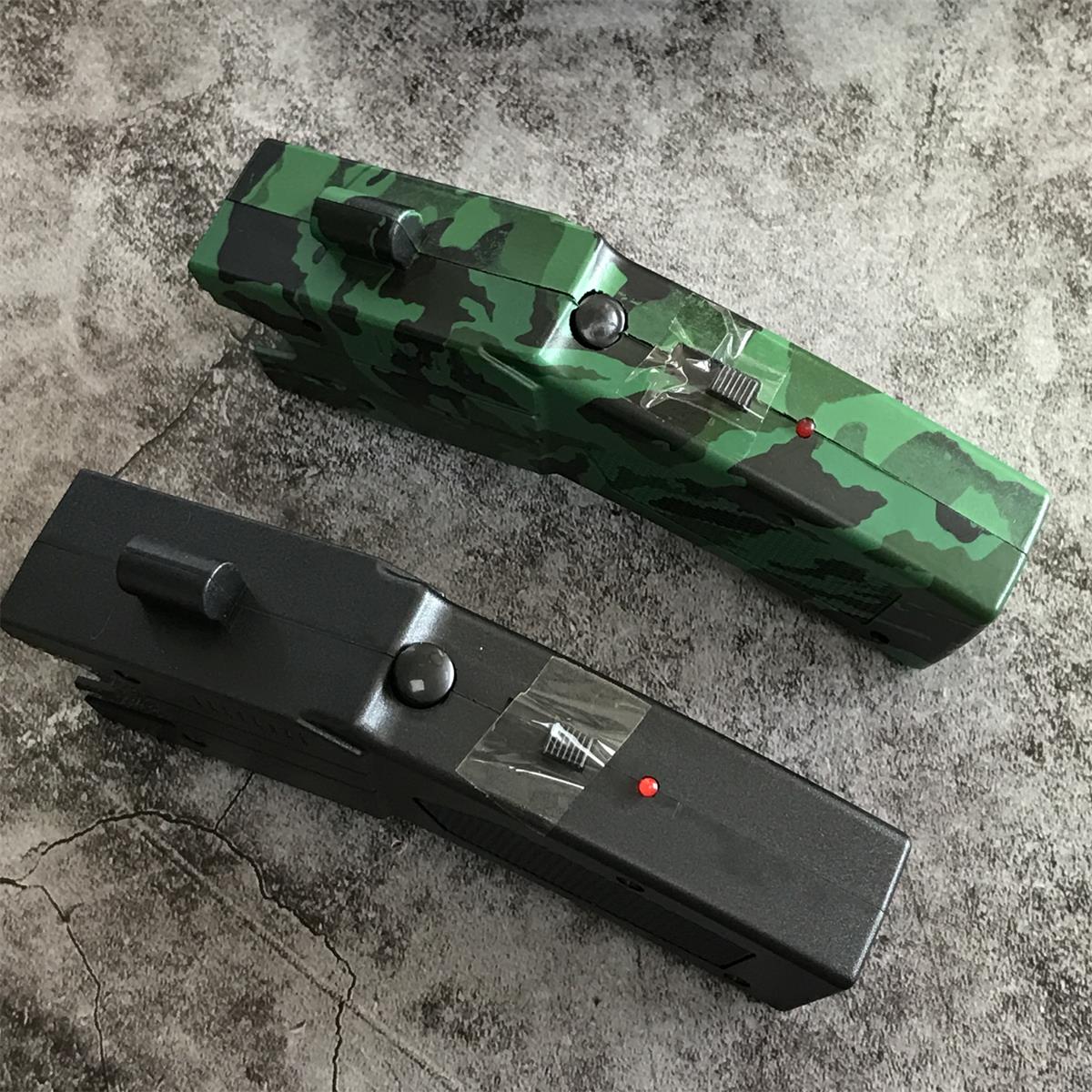 Top view of the green camouflage and black stun gun units showing the raised safety and launch toggles, round button and red LED indicator