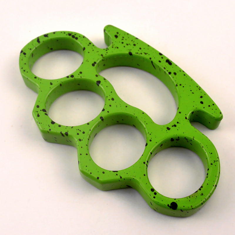 A lime green knuckle duster with black splatter paint shown at an angle on a white surface, displaying its thickness and rounded edges.