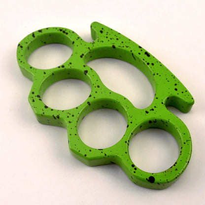 A lime green knuckle duster with black splatter paint shown at an angle on a white surface, displaying its thickness and rounded edges.