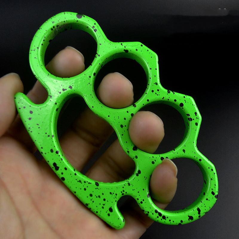 A neon green knuckle duster with black splatter paint held in an open hand, fingertips through the four holes, against a black background.