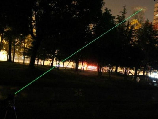 Green laser beam stretching across a night sky above trees and buildings