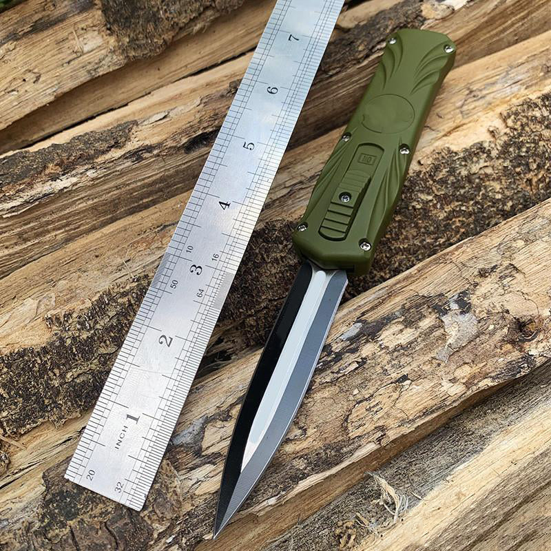 Green automatic OTF pocket knife with metal ruler on wooden logs for size reference