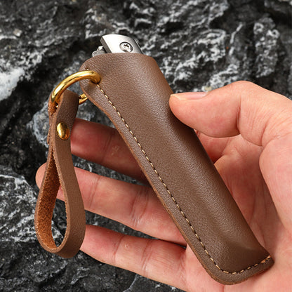Hand holding a brown leather sheath with a closed folding knife inside, brass D-ring and leather loop visible, against dark rock