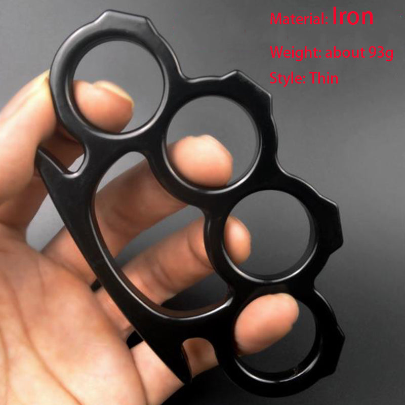Black thin iron four-finger knuckle duster held in a hand, showing four round finger holes and a pointed lower end