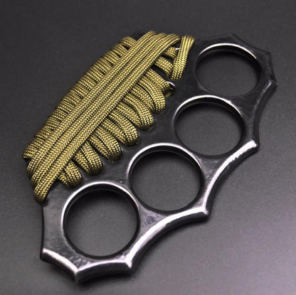 Angled overhead view of the black zinc alloy knuckle duster with four finger holes and olive-green paracord woven across the grip.