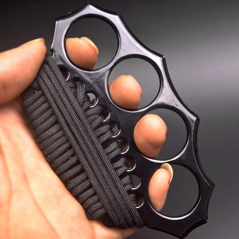 Hand holding the black knuckle duster with black paracord woven through the lower edge holes, with no packaging in frame.