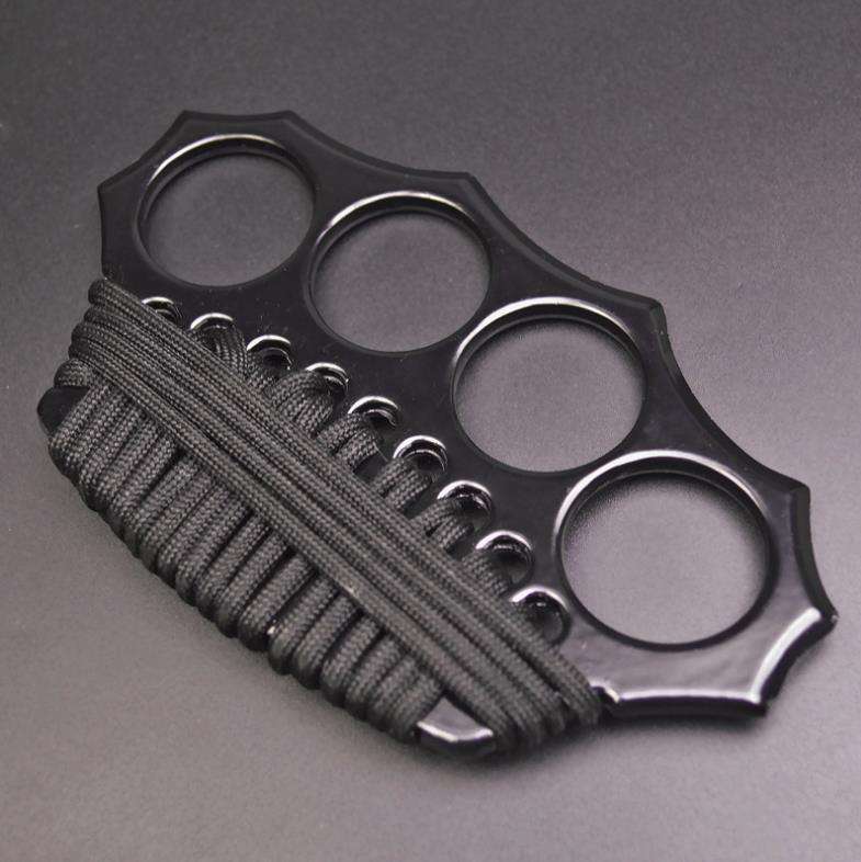 Three-quarter overhead view of the black knuckle duster with four finger holes in an arc and black paracord woven through the lower edge holes.