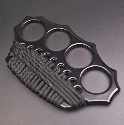 Three-quarter overhead view of the black knuckle duster with four finger holes in an arc and black paracord woven through the lower edge holes.