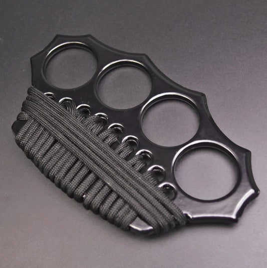 Three-quarter overhead view of the black knuckle duster with four finger holes in an arc and black paracord woven through the lower edge holes.
