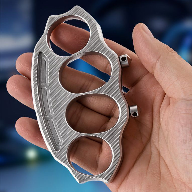 Knuckle duster held in palm showing four finger holes and diagonal machined texture