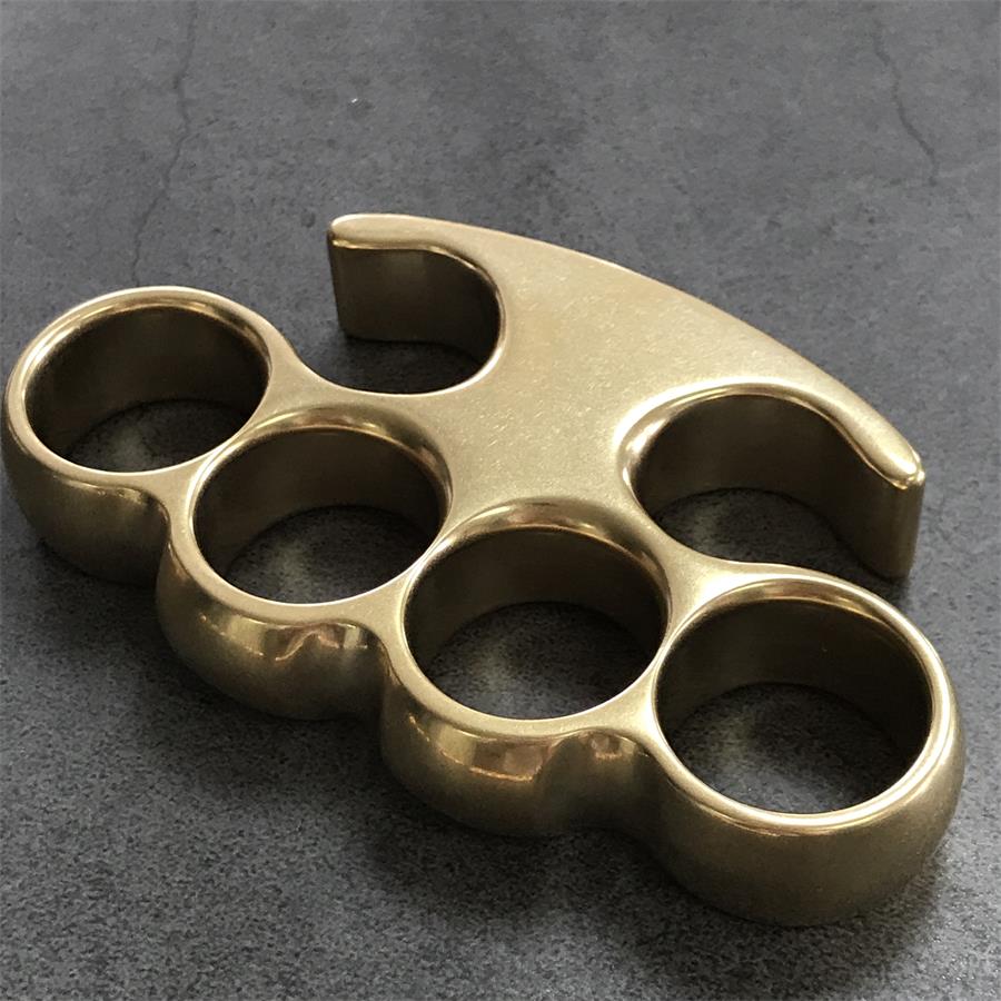 Large brass knuckle duster with claw-tip frame and four round holes, stonewashed finish on a gray concrete surface