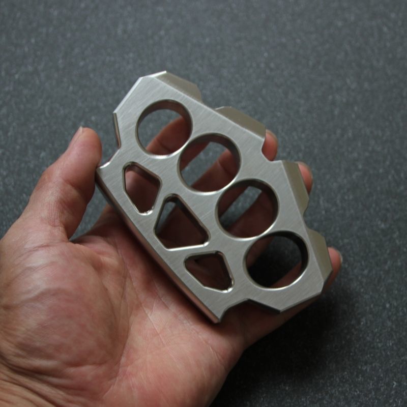 Hand holding the maple leaf shaped stainless steel knuckle duster from the side.